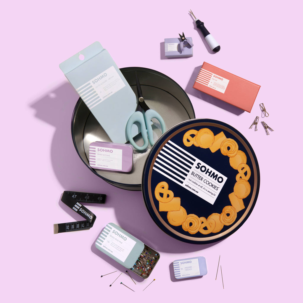 Collection of SOHMO products including cookies, scissors, and packaging on a pink background