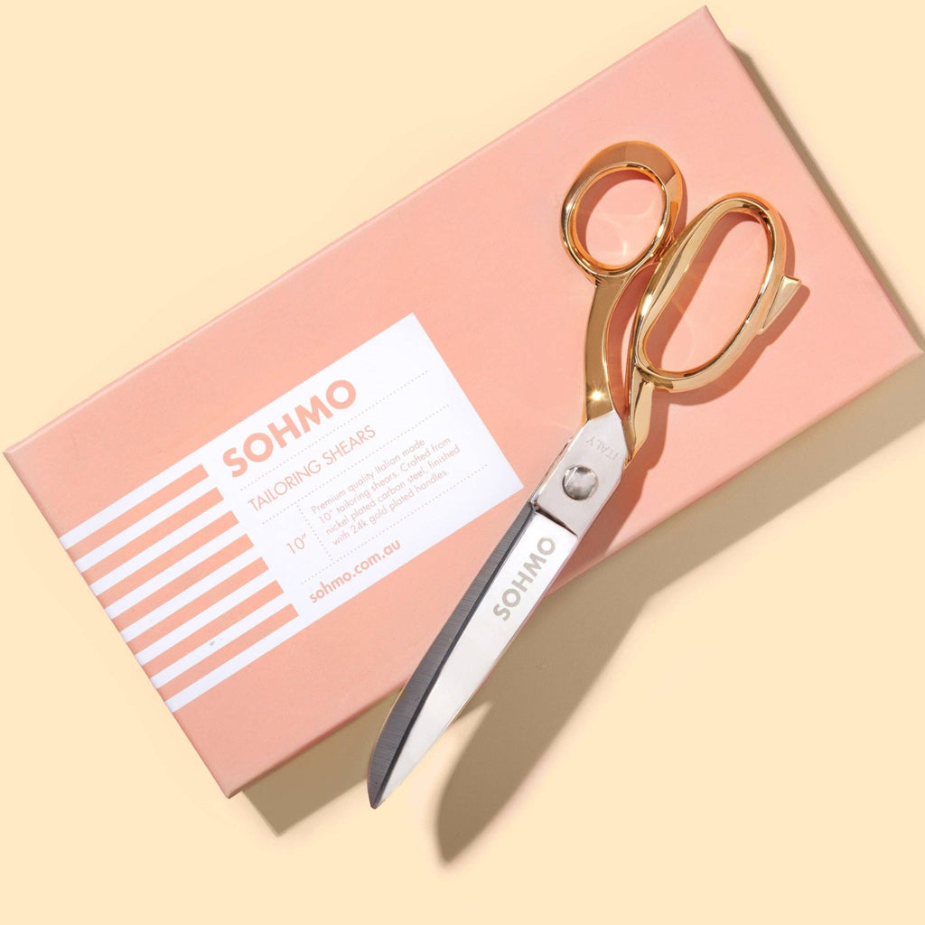 Gold scissors on a pink box with 'SOHMO' branding on a beige background