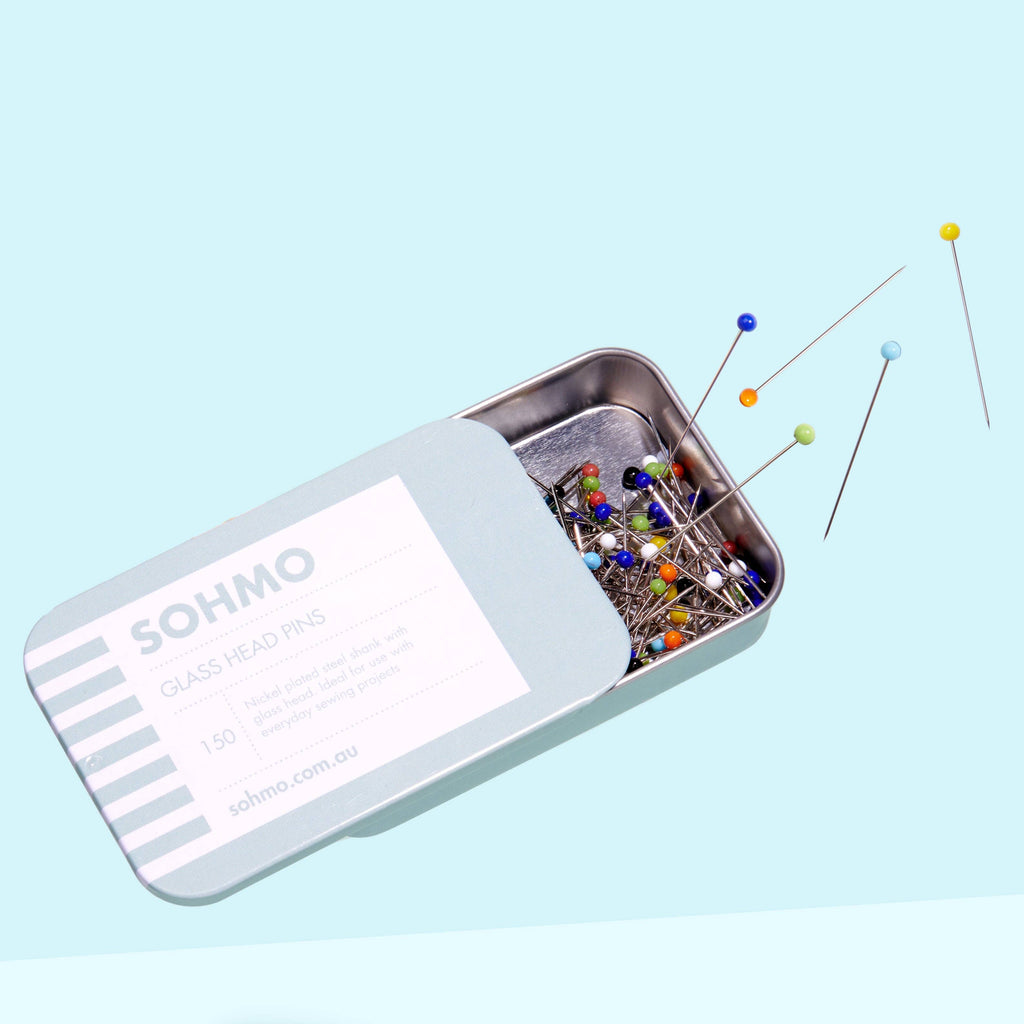 Small metal tin filled with colorful pins on a light blue background