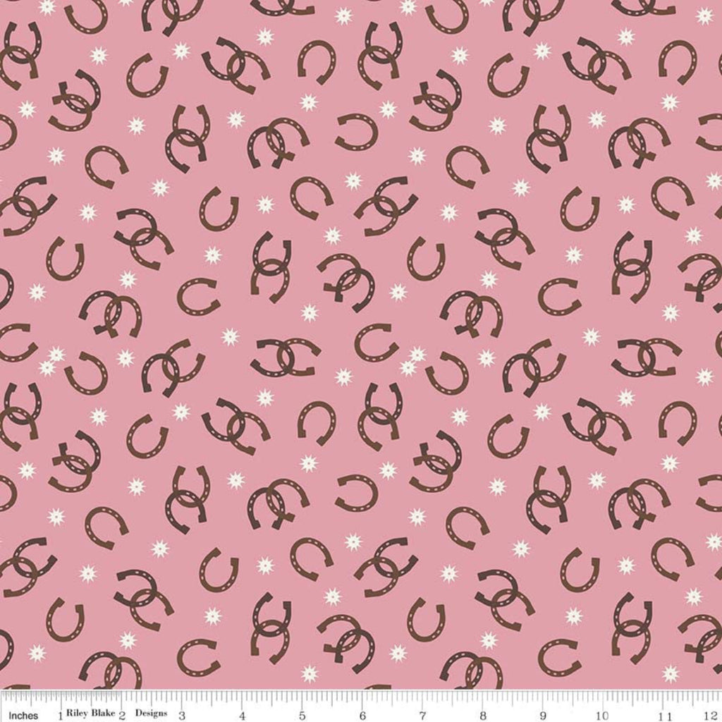 A piece of pink fabric with a pattern of horseshoes and small white dots.