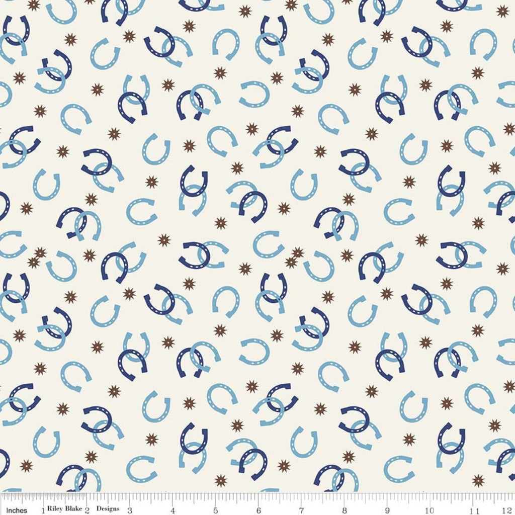 A fabric featuring a pattern with blue horseshoes and brown accents on a white background, with a ruler at the bottom for scale.