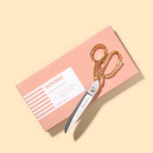 Gold scissors on a pink box with 'SOHMO' branding on a beige background