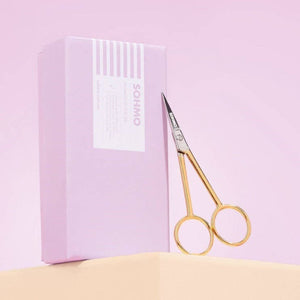 Gold scissors with a pink box on a light pink background