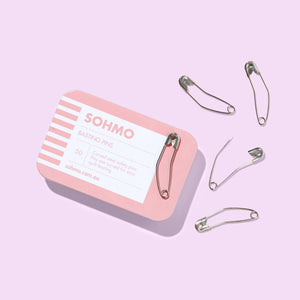 Set of safety pins with a pink and white SOHMO container on a light purple background