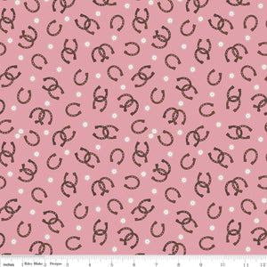A piece of pink fabric with a pattern of horseshoes and small white dots.